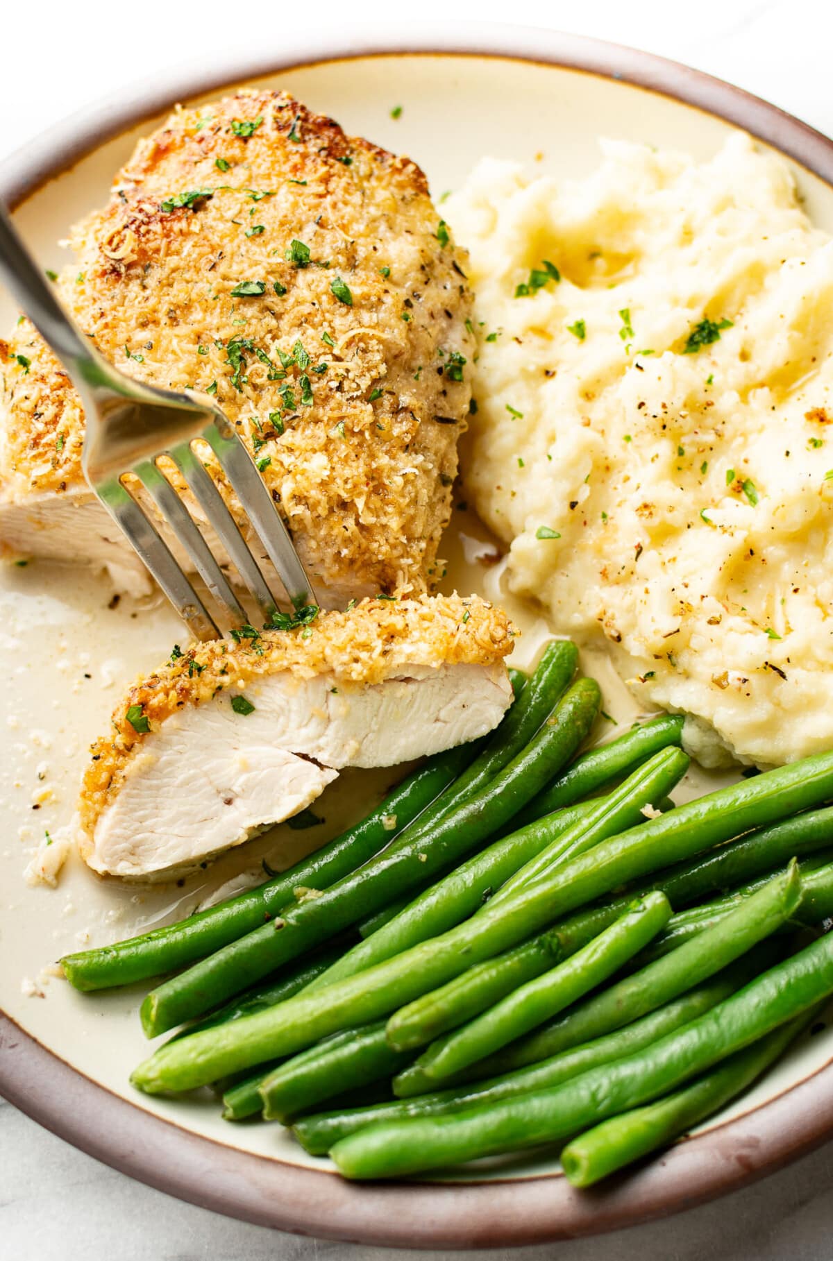 a plate with baked parmesan chicken, mashed potatoes, green beans, and a fork