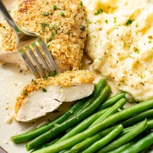 a plate with baked parmesan chicken, mashed potatoes, green beans, and a fork
