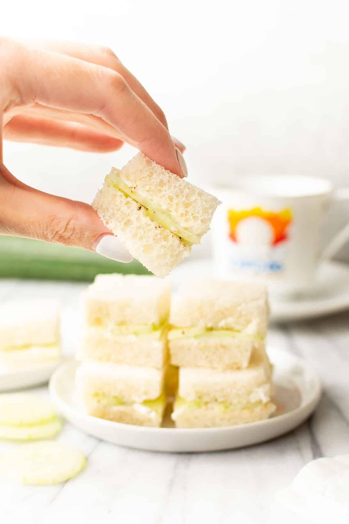 a female hand holding a cucumber tea sandwich